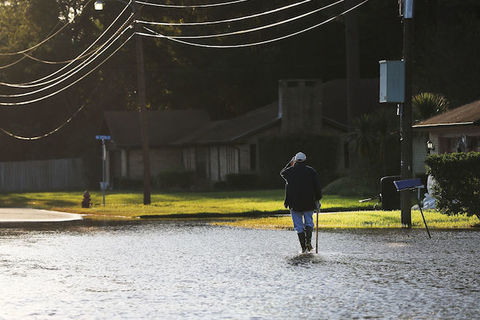 An outdoor shot of a Black man walking through flooded streets towards a house