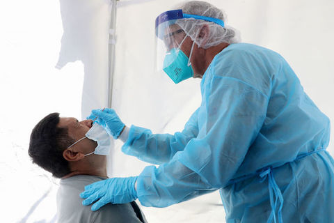 A seated man in a mask gets a nasal test for coronavirus from a masked doctor in blue scrubs.