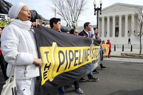 A line of activists stand in front of Supreme Court holding a banner that reads "The Pipeline Stops"
