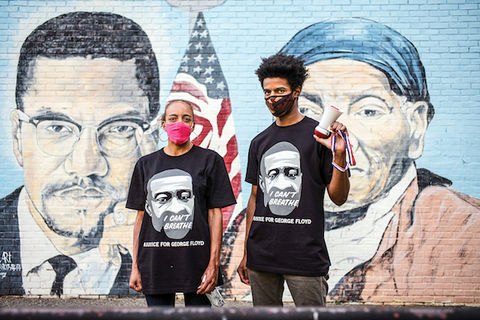 Two protesters stand in front of a painted mural of Malcolm X and Harriet Tubman.