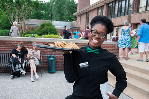 Black Waitress. Young Black woman with a dark Afro wearing a green bow tie and black shirt and pants holding a platter of cookies.