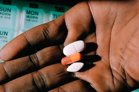 A Black hand palm facing up with three pills, a white oblong pill, an orange capsule and a white diamond shaped pill