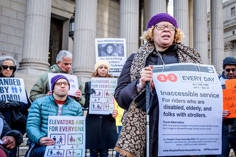 Disability Justice. A group of protestors standing outside of a court house hold signs calling for better access to the subway.