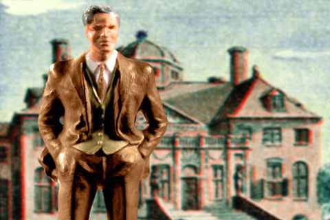 A figurine of a man in a suit stands in front of a backdrop of a house.