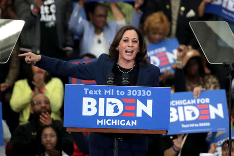 Kamala Harris stands at a podium with BIDEN written across the front. 