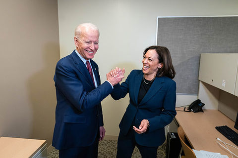 Joe Biden and Kamala Harris. Older white man with gray hair wearing blue suit hi-fiving Black woman wearing blue suit.