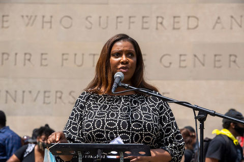 Black woman stands at a podium in front of a crowd and speaks into a microphone. 
