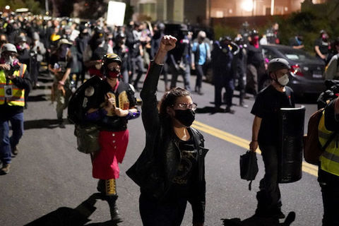 A large group of protesters march in the street, one hold a fist in the air. 