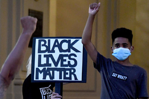 Protest. Young Black boy wearing face mask and blue Tee shirt stands with raised fist in front of sign reading: Black Lives Matter.