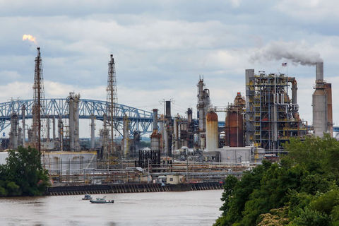 View across a bridge of an oil refinery with smoke coming out of stacks.