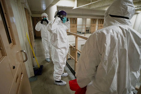 COVID19 Prisons. Men wearing white hazmat suits cleaning a prison cell.