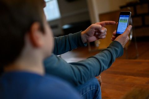 Eight year old boy in foreground watching his father hold a cell phone with his school lessons on it.