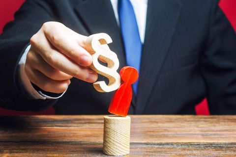 White man in suit holding piece which is knocking symbol of person off a pedastal.