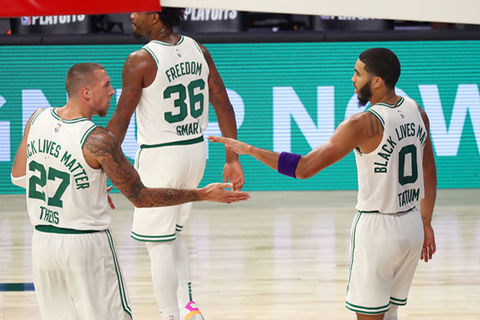 Boston Celtics-Three basketball players wearing white jerseys with green lettering walking away from the camera on court.