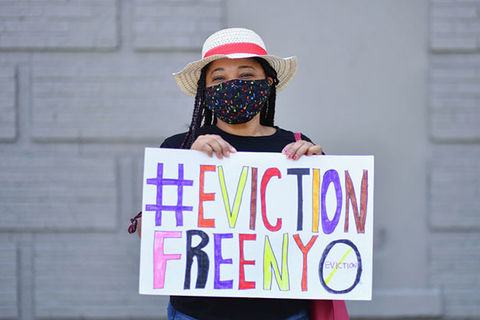 Eviction Protest. Young woman wearing a hat and black face mask holds colorful sign reading: #EvictionFreeNYC