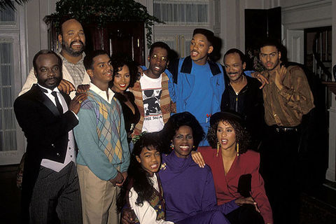 Fresh Prince of Bel Air cast. A group of Black men and women of all ages huddle for a group photo inside of a house.