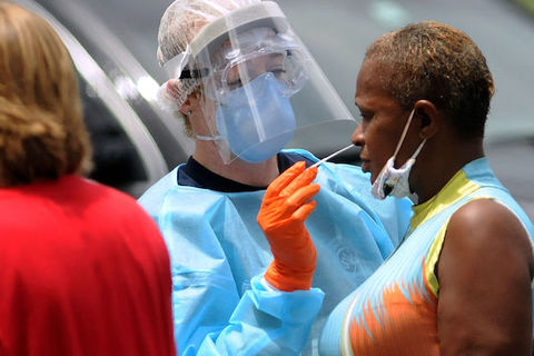 Black woman receives swap COVID-19 test from a person wearing PPE. 