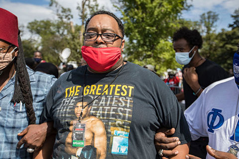 Jacob Blake Sr. Black man with short dark hair and glasses wearing red face mask and black Tee with Muhammed Ali in a boxing stance.
