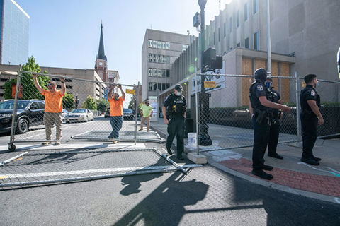 LMPD. Men in police uniforms and construction outfits erect fencing on a street.