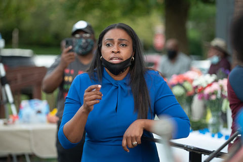 Lovely Warren. Black woman with long dark hair wearing blue dress and black face mask.