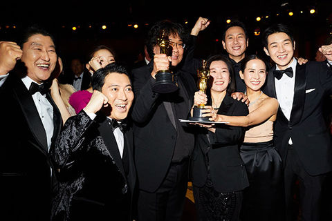 Parasite. Group of Korean men and women dressed in formal black attire holding an Oscar award and cheering.