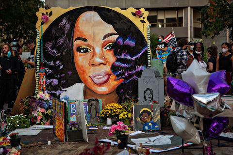 painting of Black woman with long black hair is surrounded by flowers and other tributes. 