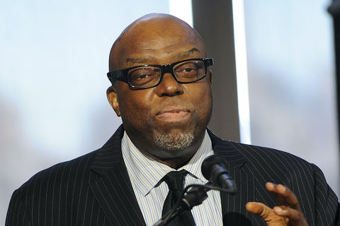Image of bald, bespectacled Black man speaking at microphone