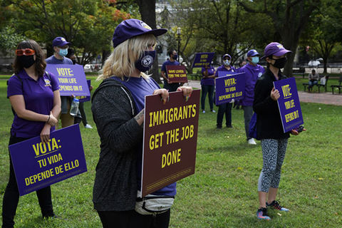 Service Employee International Union. People wearing purple shirts, masks, hats holding signs on a lawn as they socially distance.