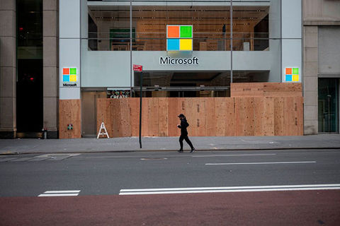 Microsoft. Boarded up storefront with windows logo  and person wearing all black running by.