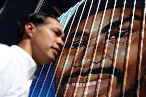 Oscar Grant. Latinx man with short dark hair wearing white shirt stands in front of mural of black man.