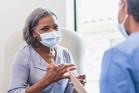 Older Black woman with short gray hair wearing a blue mask and purple top standing in front of white man wearing a blue mask and blue shirt.