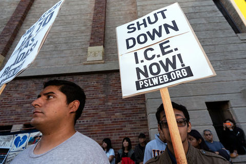 A black and white protest sign reads, Shut Down I.C.E. Now!