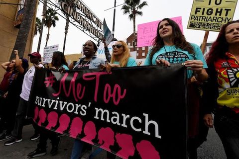 a group of women wearing blue shirts stand in a row and hold a large banner that reads, Me Too Survivors March