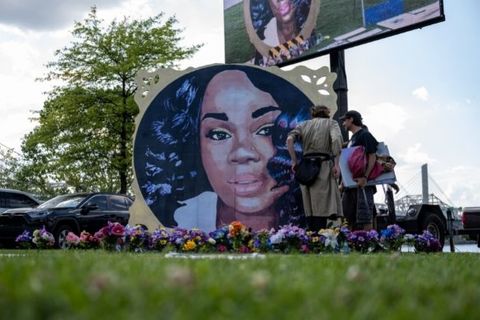 A painted mural of Breonna Taylor surrounded by flowers on a grassy lawn.