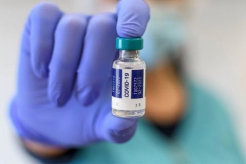 Close-up selective focus image of medical worker with blue gloves holding covid vaccine vial.