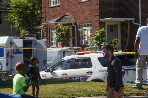  A woman sits with her child behind police tape watching a shooting investigation unfold.