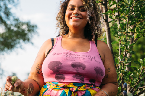 A photo of adrienne maree brown in a pink tank-top that reads "Be Beautiful Everyday"