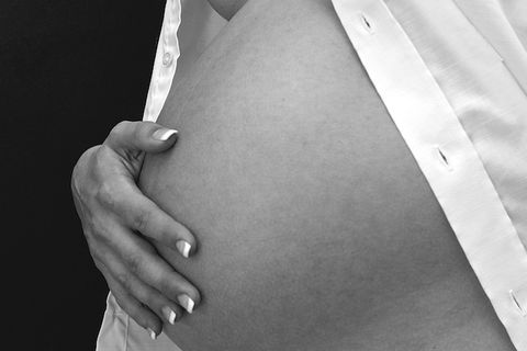 Black-and-white image of a bare pregnant stomach with a white shirt around it and a hand resting on stomach
