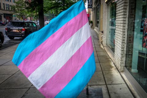 Trans flag hanging above a city street. Flag has blue, pink and white stripes.